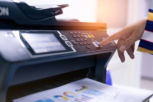 Office worker print paper on multifunction laser printer. Copy, print, scan, and fax machine in office. Modern print technology.  Photocopy machine. Document and paper work. Professional scanner.